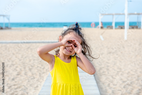 Adorable curly toddler girl in a yellow dress plays on the white sand beach 