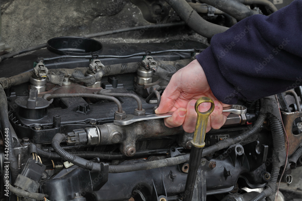 Worker fixing modern common rail diesel engine, closeup of hand with spanner tool, rail, pipeline and injectors Worker fixing modern common rail diesel engine, closeup of hand with spanner tool, rail, pipeline and injectors