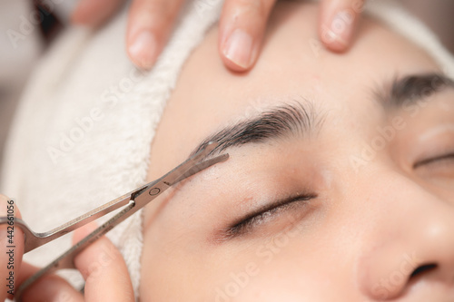 Eyebrows trimming service in spa salon, Face hair cutting and trim with small scissor tool for facial beauty women closeup. photo