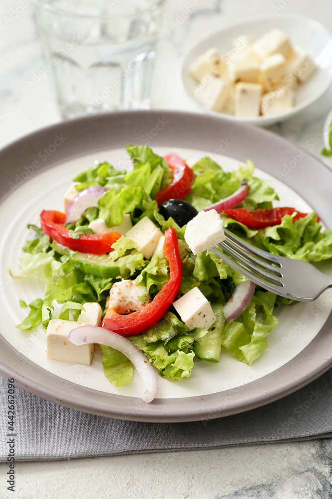 Plate with fresh Greek salad on light background