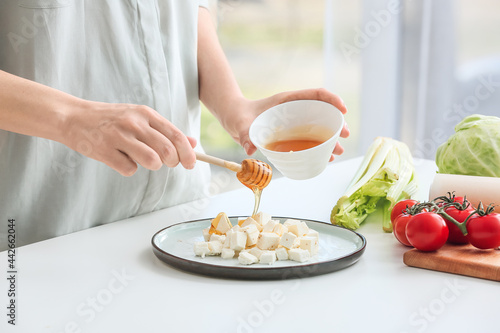 Woman pouring honey onto feta cheese on plate  closeup