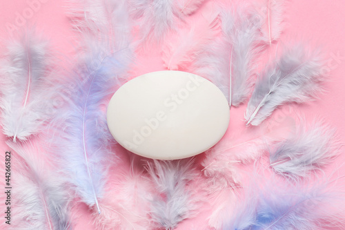 Soap bar and feathers on color background