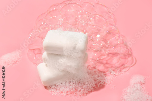 Stack of soap bars with foam on color background