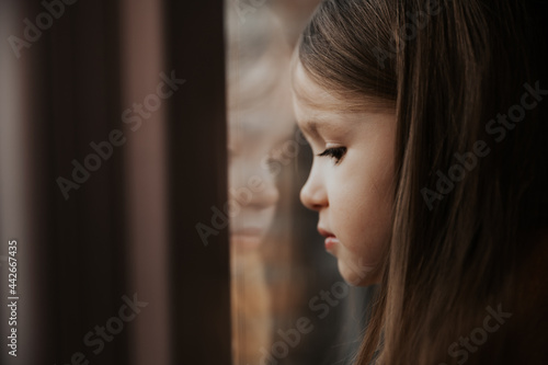 A little girl on the windowsill looks out the window from the apartment in a high-rise building