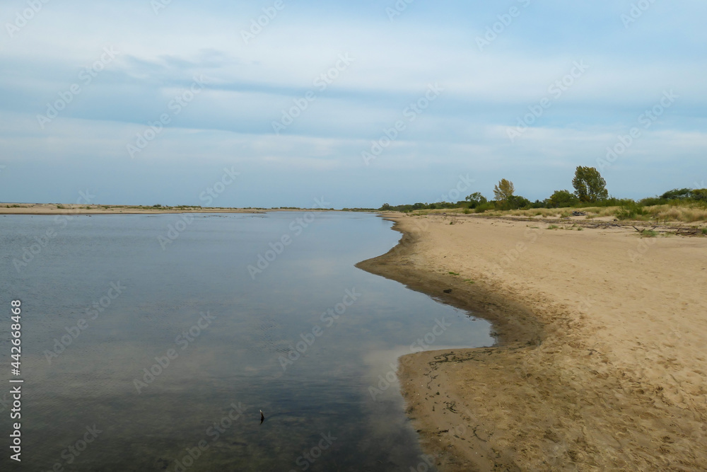 The coastal line of a sandy beach by the Baltic Sea on Sobieszewo island, Poland. The sea is gently waving. A bit of overcast. Solitude and serenity