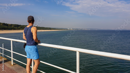 Fotografie A man in shorts and full-cap standing at the pier by the Baltic Sea side in Poland