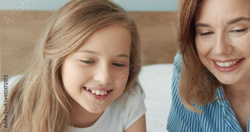 Close up of beautiful happy caucasian woman talking with her preschool daughter sitting inbedroom on weekend morning. photo