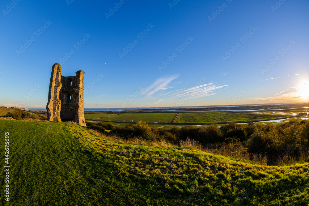 Hadleigh Castle, Essex, England on the left with the sun setting on the right clear blue sky with backlit grass fisheye lens