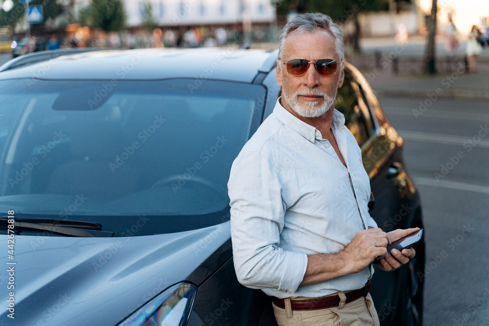 Senior man standing near his SUV car and holding smartphone. Middle aged man portrait outdoors near his car Senior man standing near his SUV car and holding smartphone. Middle aged man portrait outdoors near his car