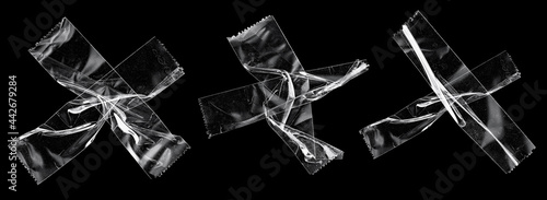 transparent sticky tapes forming the letter x or overlapping each other on black background, crumpled plastic snips, poster design overlays. photo