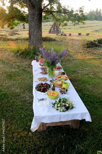 Midsummer food table.Table filled with drinks and food outside in the garden under the trees. on the table a glass vase with blue meadow flowers. Latvian LIGO festive