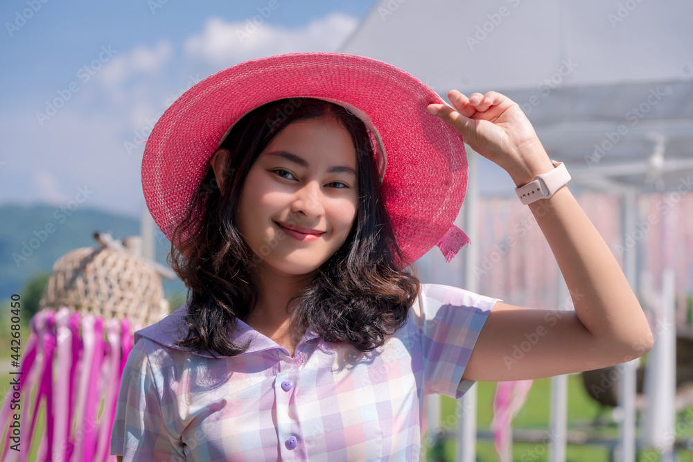 portrait of attractive Asian woman with casual cloth and pink hat happy smiling in garden in sunny day, pretty girl relax on vacation in summer