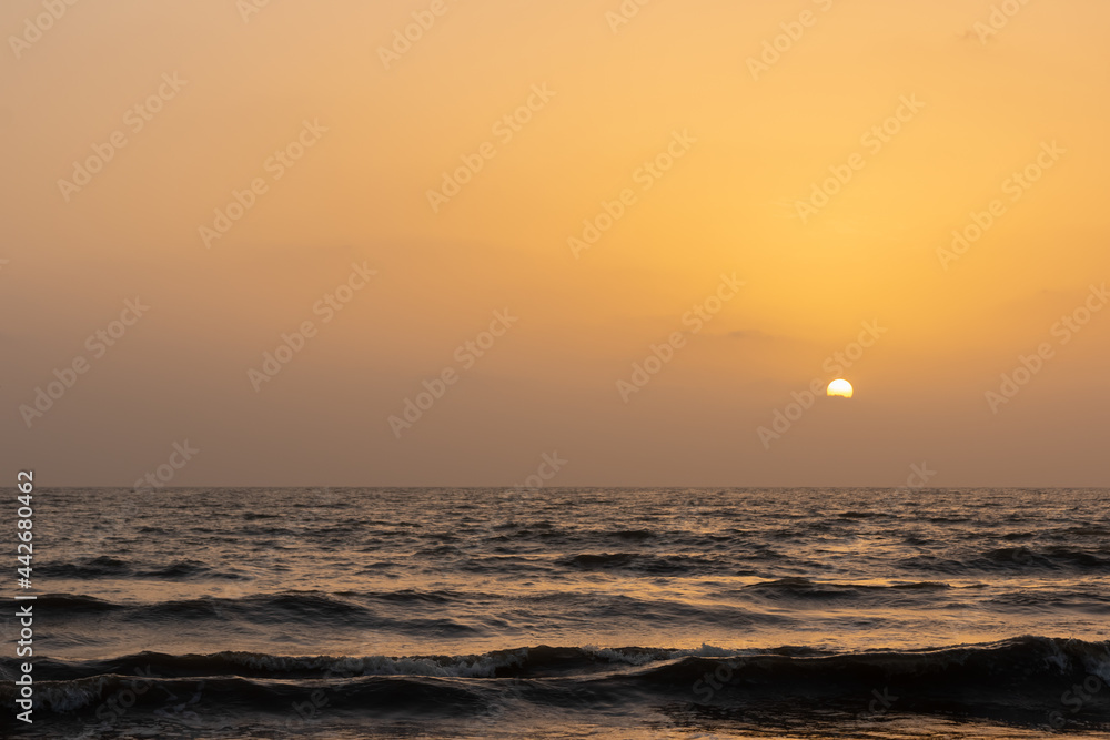 Fototapeta premium A view of sun setting in the horizon and waves in the ocean