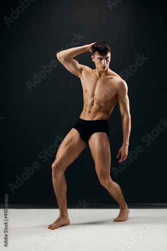 man with a pumped-up muscular body in black shorts posing against a dark background