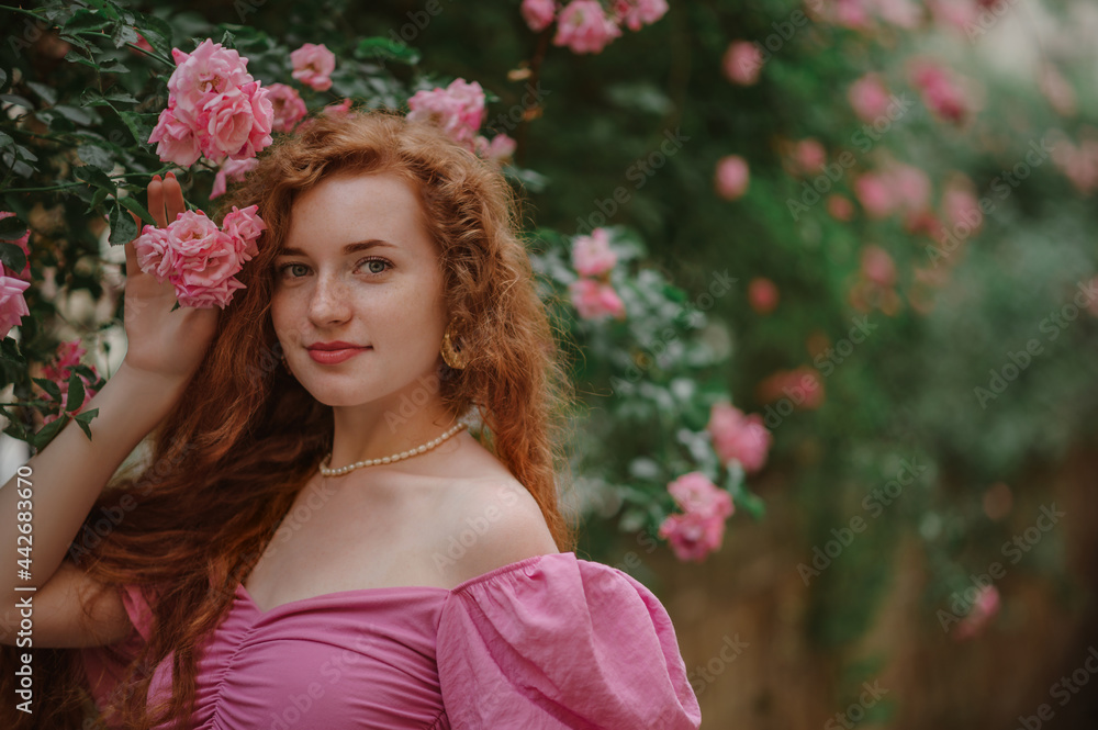 Beautiful redhead freckled woman with long curly natural hair, posing in blooming rose garden. Beauty, hair care, summer lifestyle conception. Outdoor close up portrait. Copy, empty space for text Beautiful redhead freckled woman with long curly natural hair, posing in blooming rose garden. Beauty, hair care, summer lifestyle conception. Outdoor close up portrait. Copy, empty space for text