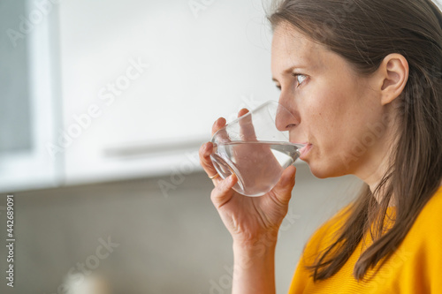 young woman drinks water at home in the kitchen. A woman escapes from thirst  very thirsty on a hot day. Compliance with the water balance. Close-up