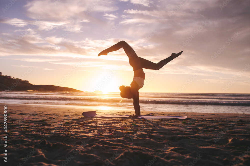 Woman doing yoga pose handstand on beach - obrazy, fototapety, plakaty 