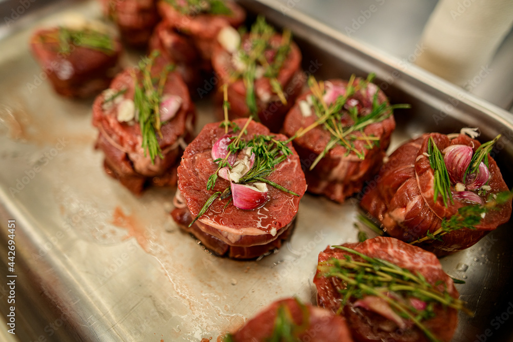 selective view of meat pieces with rosemary and spices on baking sheet selective view of meat pieces with rosemary and spices on baking sheet