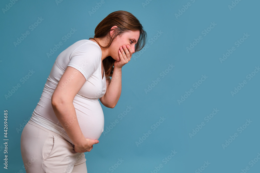 Heartburn in throat in pregnant woman, studio shot on blue background Heartburn in throat in pregnant woman, studio shot on blue background