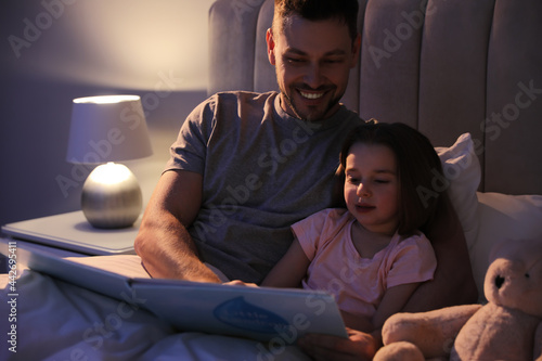Father reading bedtime story to his daughter at home photo