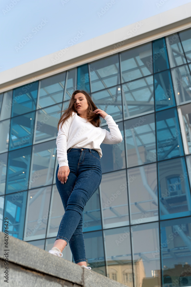Bottom view on young beautiful woman in the city. Modern building on background. Vertical frame.
