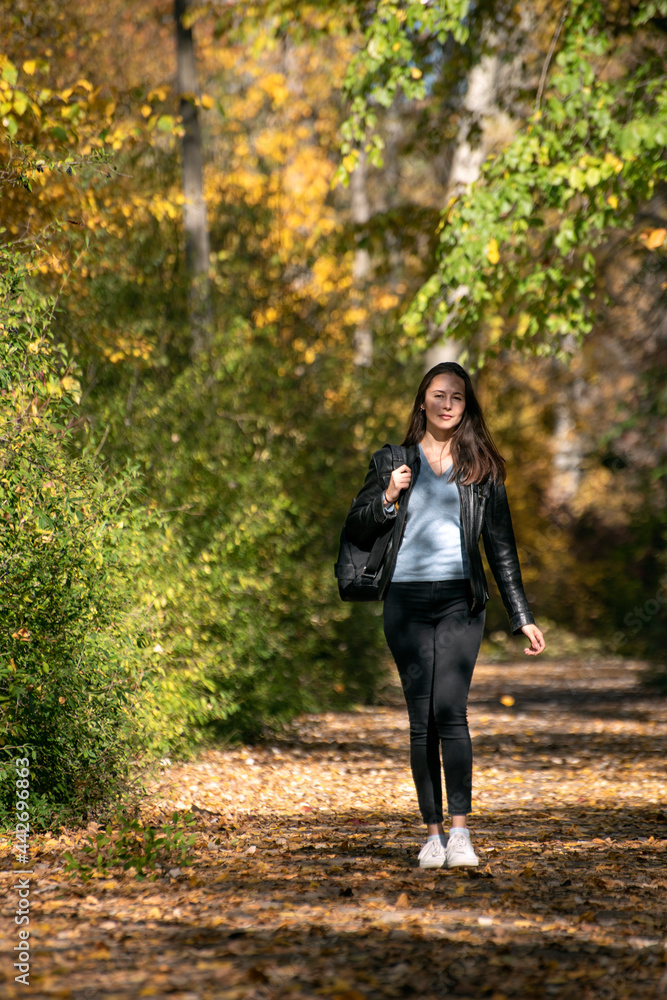 Beautiful young woman with dark hair walks along the alley of autumn park and enjoys a warm day. Lonely girl in forest Beautiful young woman with dark hair walks along the alley of autumn park and enjoys a warm day. Lonely girl in forest