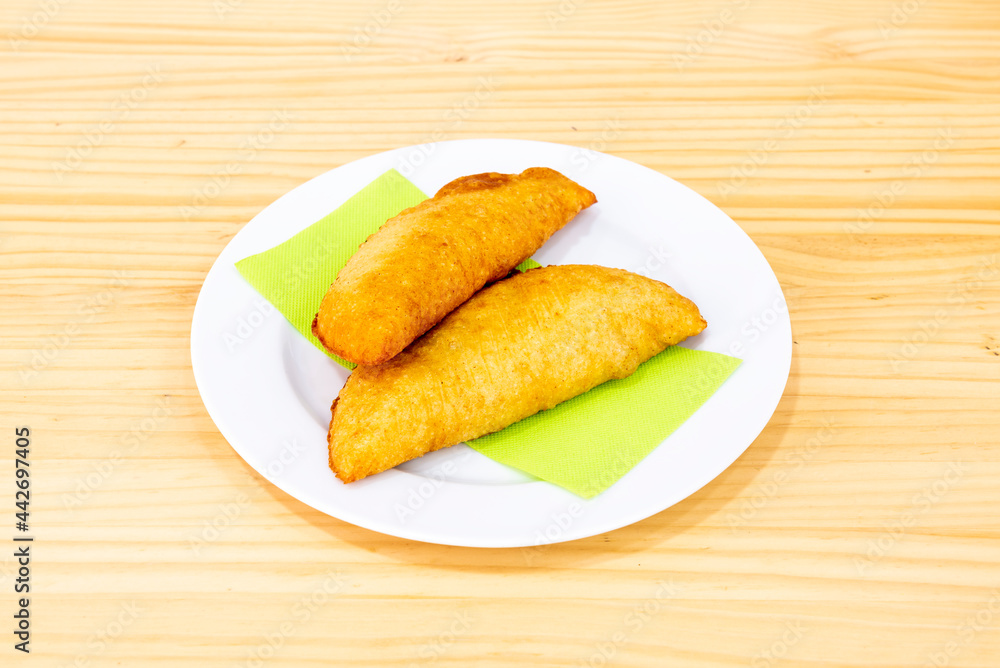 Colombian yellow corn empanadas stuffed with chicken stew with red peppers on white plate and wooden table Colombian yellow corn empanadas stuffed with chicken stew with red peppers on white plate and wooden table