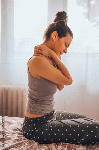 Woman suffering from back pain while sitting on bed.