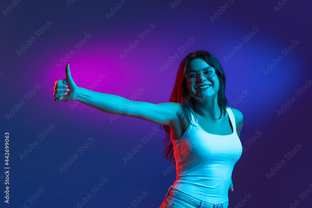 Caucasian young woman's portrait on dark studio background in neon. Concept of human emotions, facial expression.