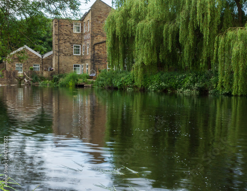 Hirst Mill and the nearby willow trees reflected in the waters of the River Aire in Hirst Wood