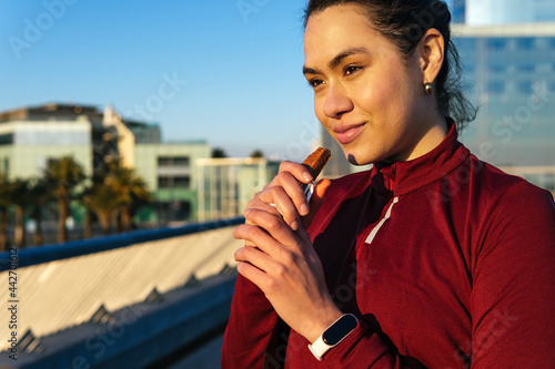 Sportswoman eating protein bar on street