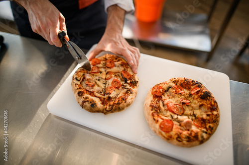 selective focus of pizza on cutting board that chef cuts into pieces with cutter