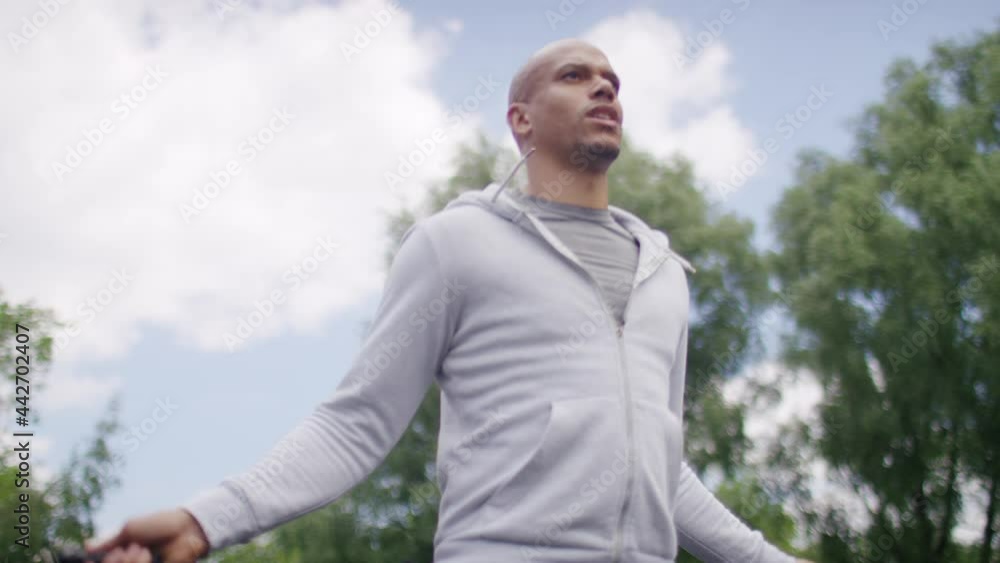 Handheld shot of young man skipping with a jump rope outside in a park, in slow motion Handheld shot of young man skipping with a jump rope outside in a park, in slow motion