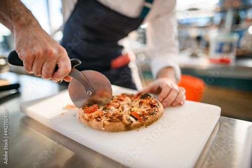 close-up of pizza on cutting board that chef cuts into pieces with cutter