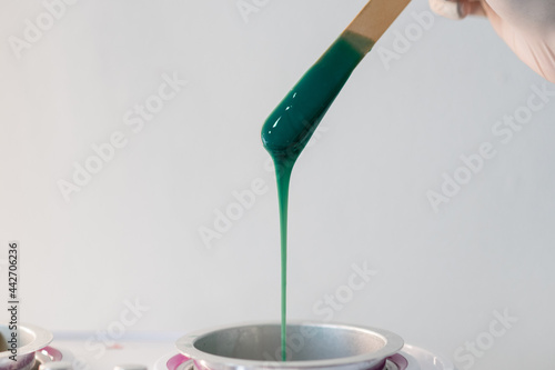 Close-up of wax heater with hot green wax and a wooden spatula © Detkov D