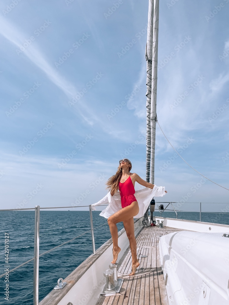 Turned back model with a perfect body in a red bikini is standing on her yacht