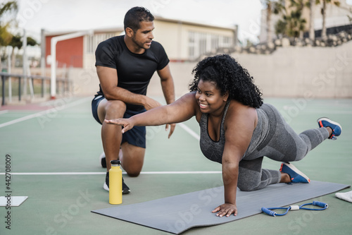 African curvy woman and personal trainer doing pilates workout session outdoor - Main focus on girl face