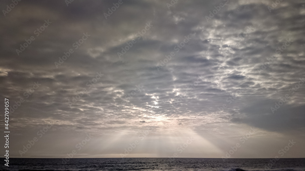 Crepuscular sun rays streaming through overcast monsoon clouds above the sea