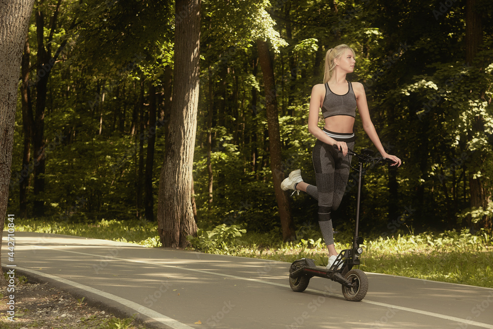 Fototapeta premium A young beautiful girl rides an electric scooter in the summer in the park, there is a free place for advertising