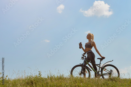 Girl on a bicycle on a background of blue sky and green grass © Юрий Дровнин