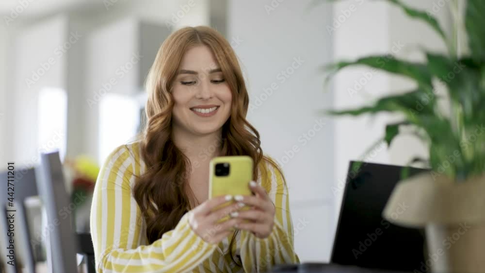 Smiling woman writing text message on smartphone while sitting at desk Smiling woman writing text message on smartphone while sitting at desk