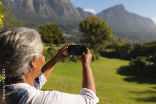 Senior african american woman taking photographs on smartphone of stunning view in sunny garden