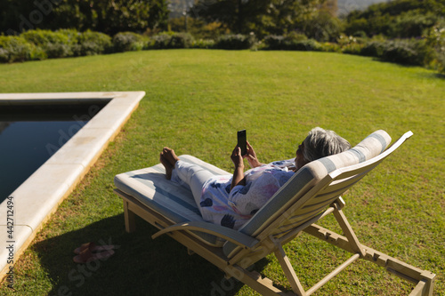 Canvas Print Senior african american woman using smartphone in deckchair by swimming pool in