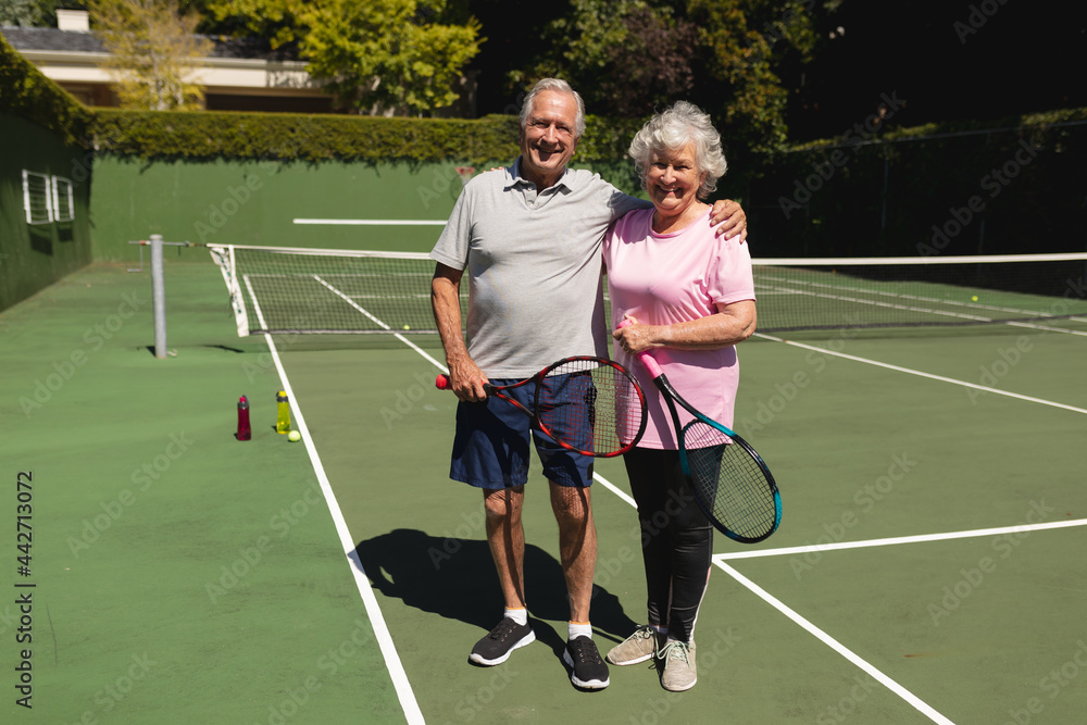 Portrait of senior caucasian couple looking at camera and smiling on tennis court