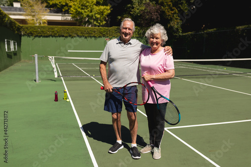 Portrait of senior caucasian couple looking at camera and smiling on tennis court