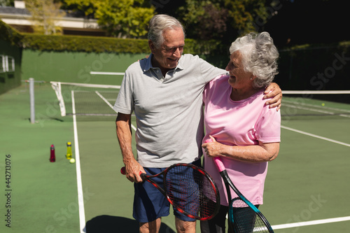 Senior caucasian couple embracing and smiling on tennis court