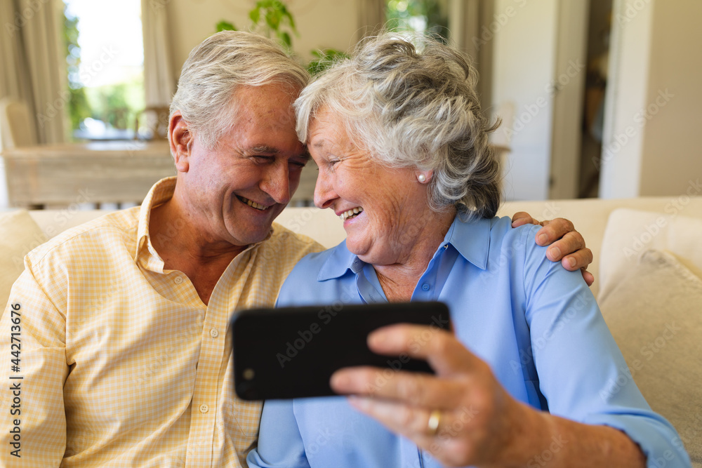 Senior caucasian couple sitting on sofa having video call using smartphone Senior caucasian couple sitting on sofa having video call using smartphone