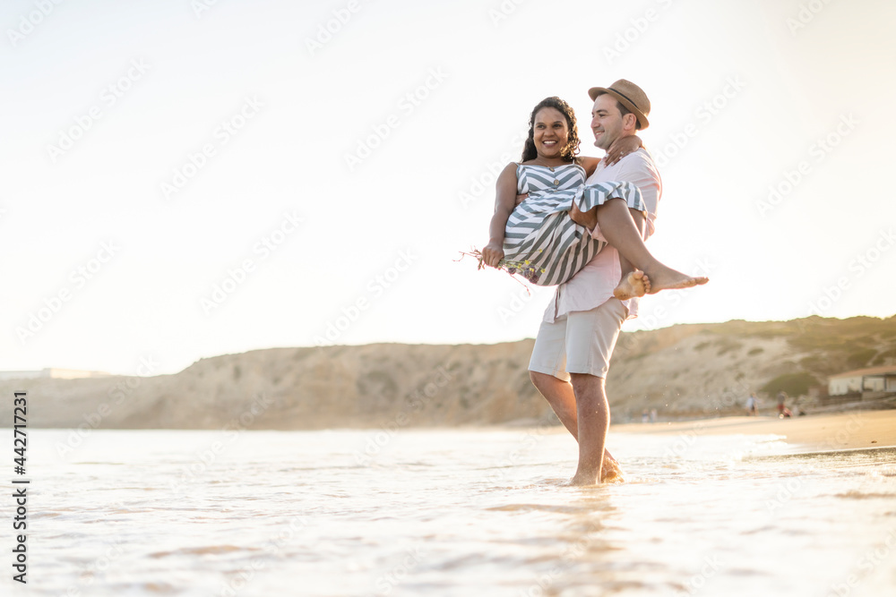 A young man carrying his beloved woman on the beach by sunset