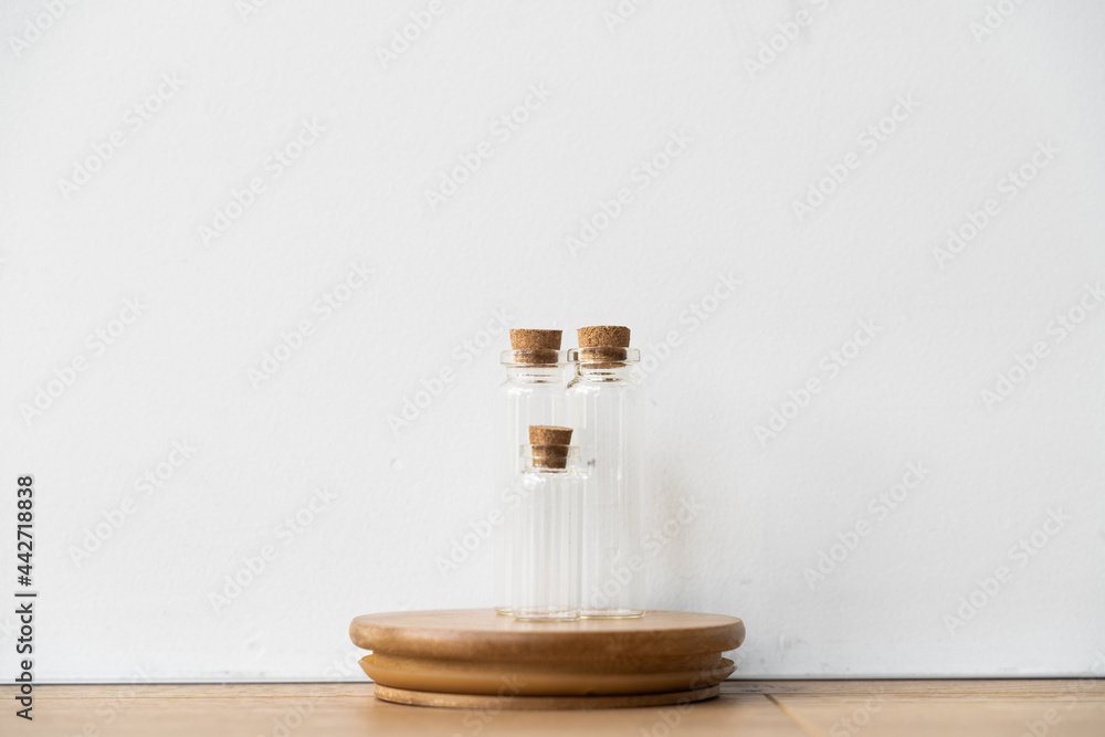 Three glass bottles with cork stopper on wooden podium with white wall background. Essential oil refilling store. Mockup template. Three glass bottles with cork stopper on wooden podium with white wall background. Essential oil refilling store. Mockup template.