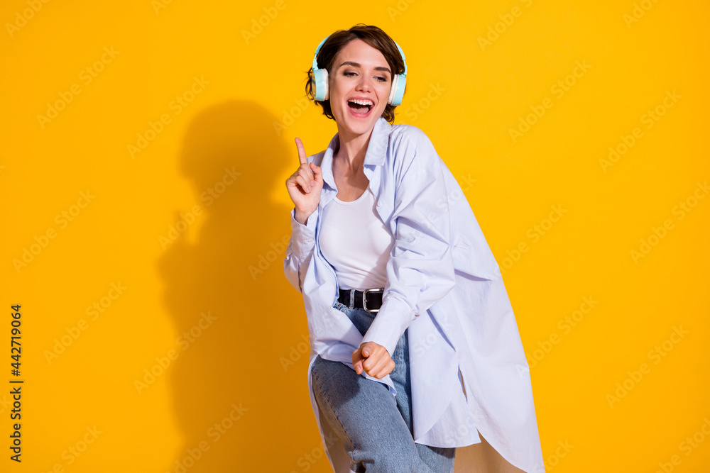 Photo portrait of smiling millennial in blue earphones hearing favorite song dancing isolated on vibrant yellow color background Photo portrait of smiling millennial in blue earphones hearing favorite song dancing isolated on vibrant yellow color background